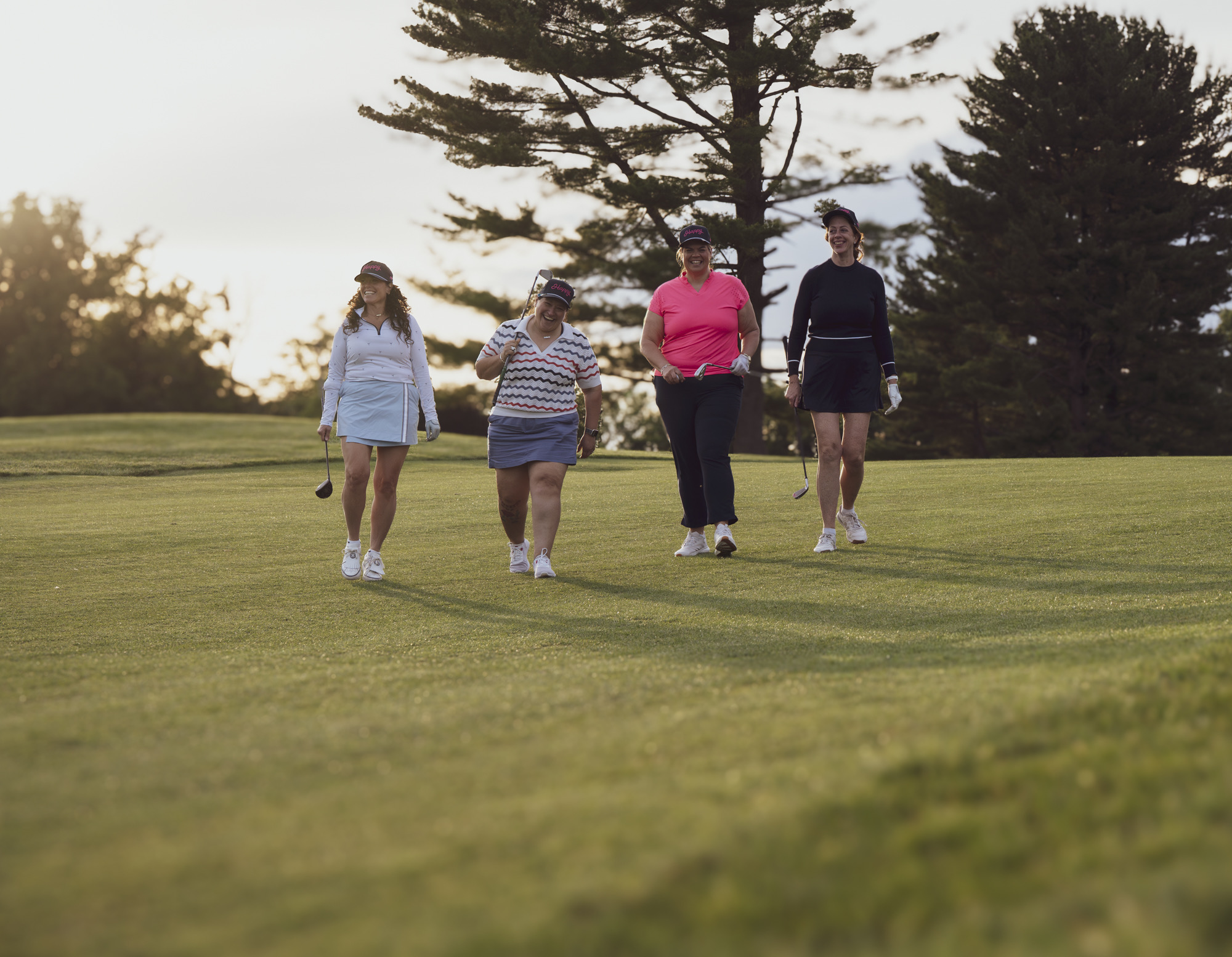 Four women walking up the fairway together at golden hour